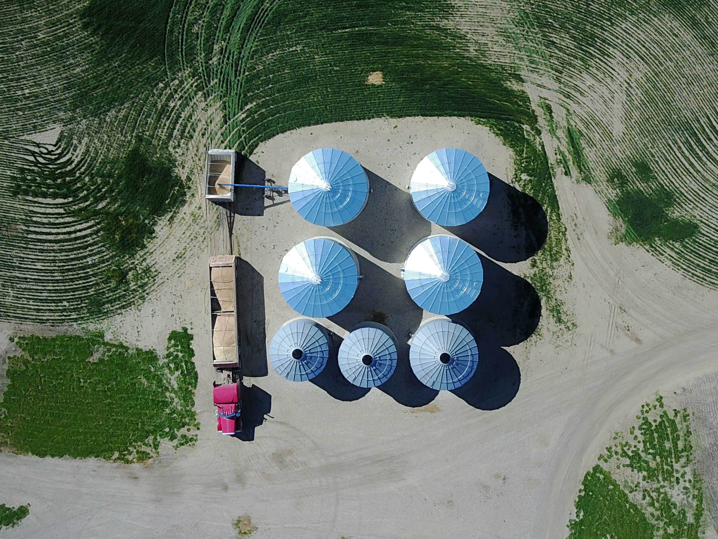 Seven grain bins and a loaded semi from directly above