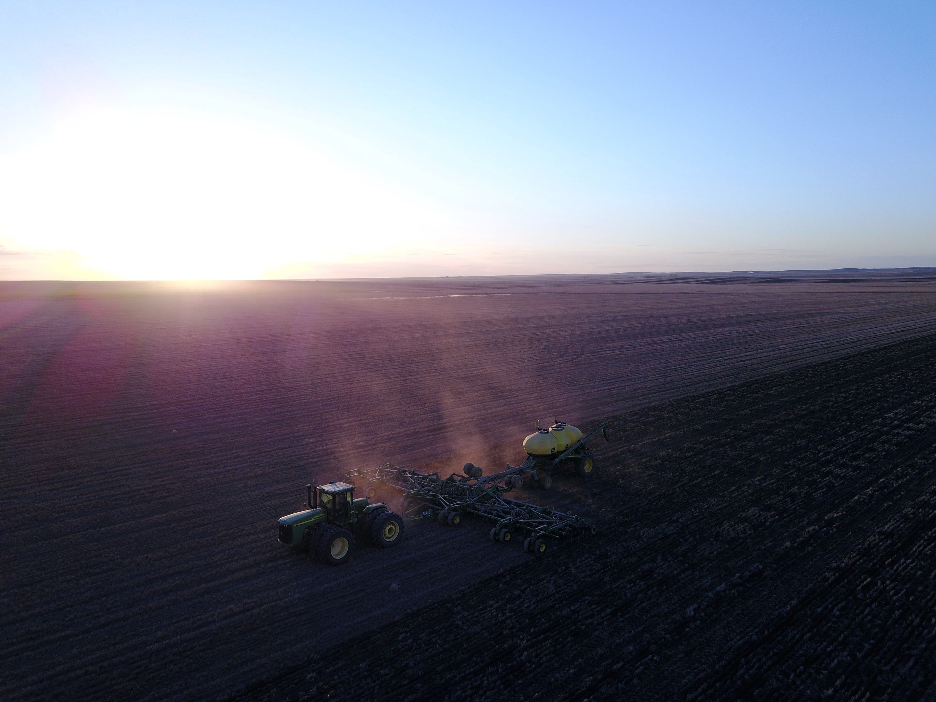 A tractor and air drill seeding at sunrise, dust rising behind it